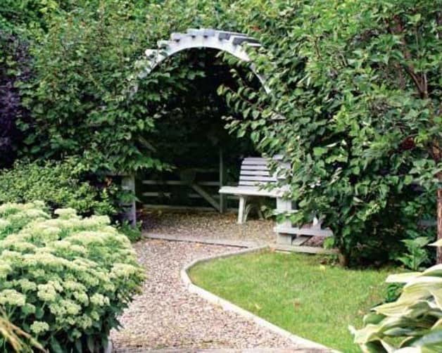 Белая деревянная арка в саду и зеленые вьющиеся растения - уголок отдыха
